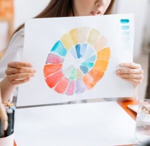 Hands holding a watercolor circle showcasing a full color palette during an art workshop setting indoors.